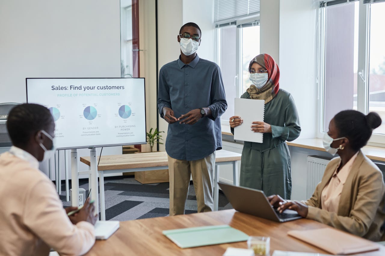 Business team presenting sales data while wearing face masks in a modern office.